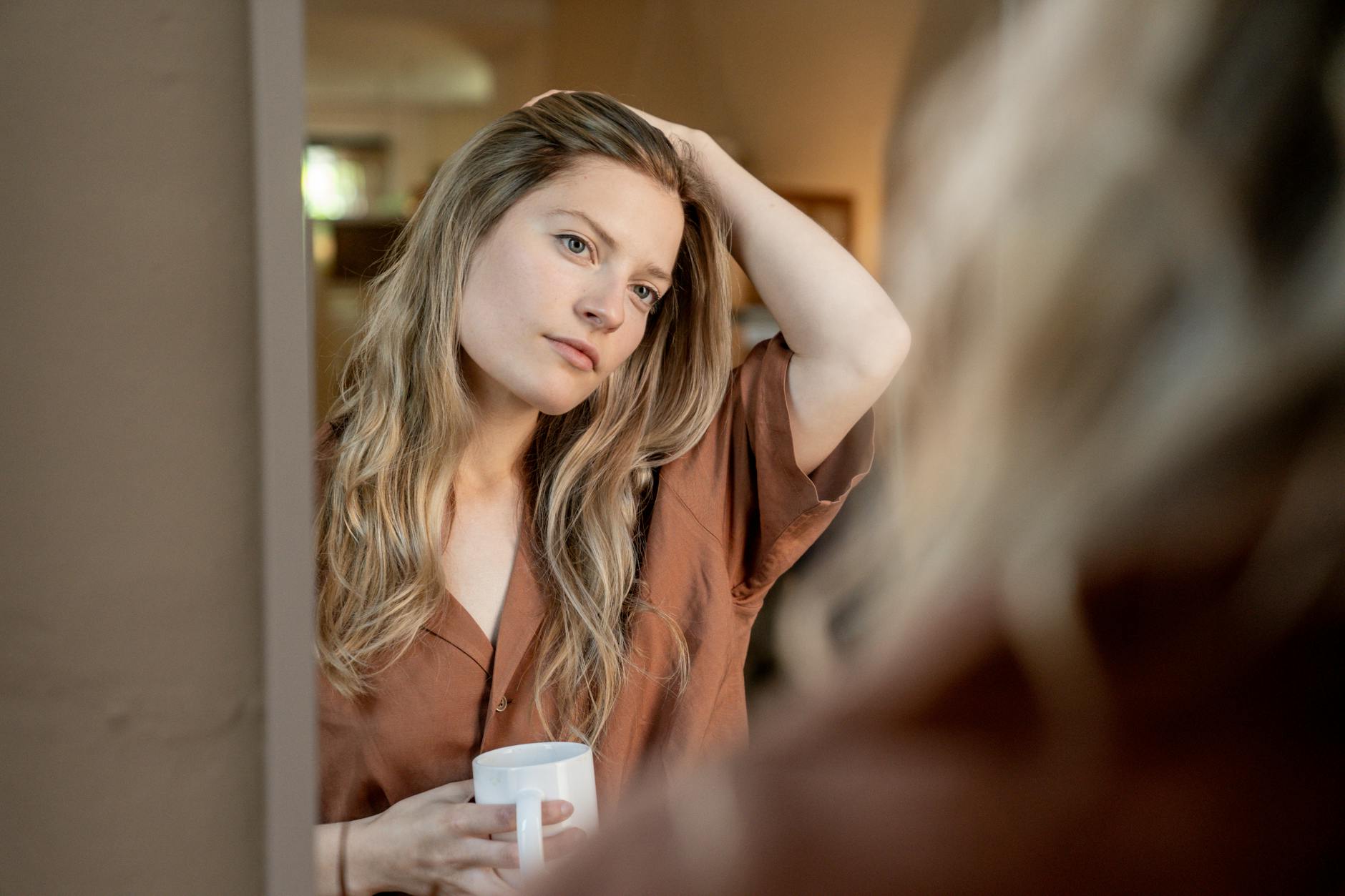 a woman looking at her reflection while holding a ceramic mug
